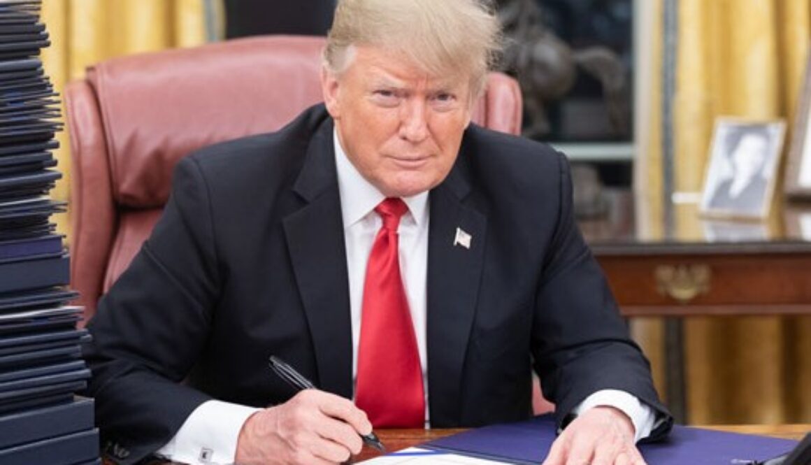 President Donald Trump sits at the Resolute Desk in the Oval Office while signing a document, accompanying coverage of the White House’s first Artificial Intelligence legislative recommendations to Congress.