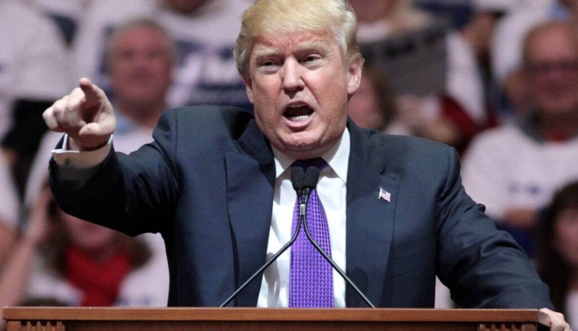 President Trump points from a rally podium during remarks calling for government equity stakes in AI companies.